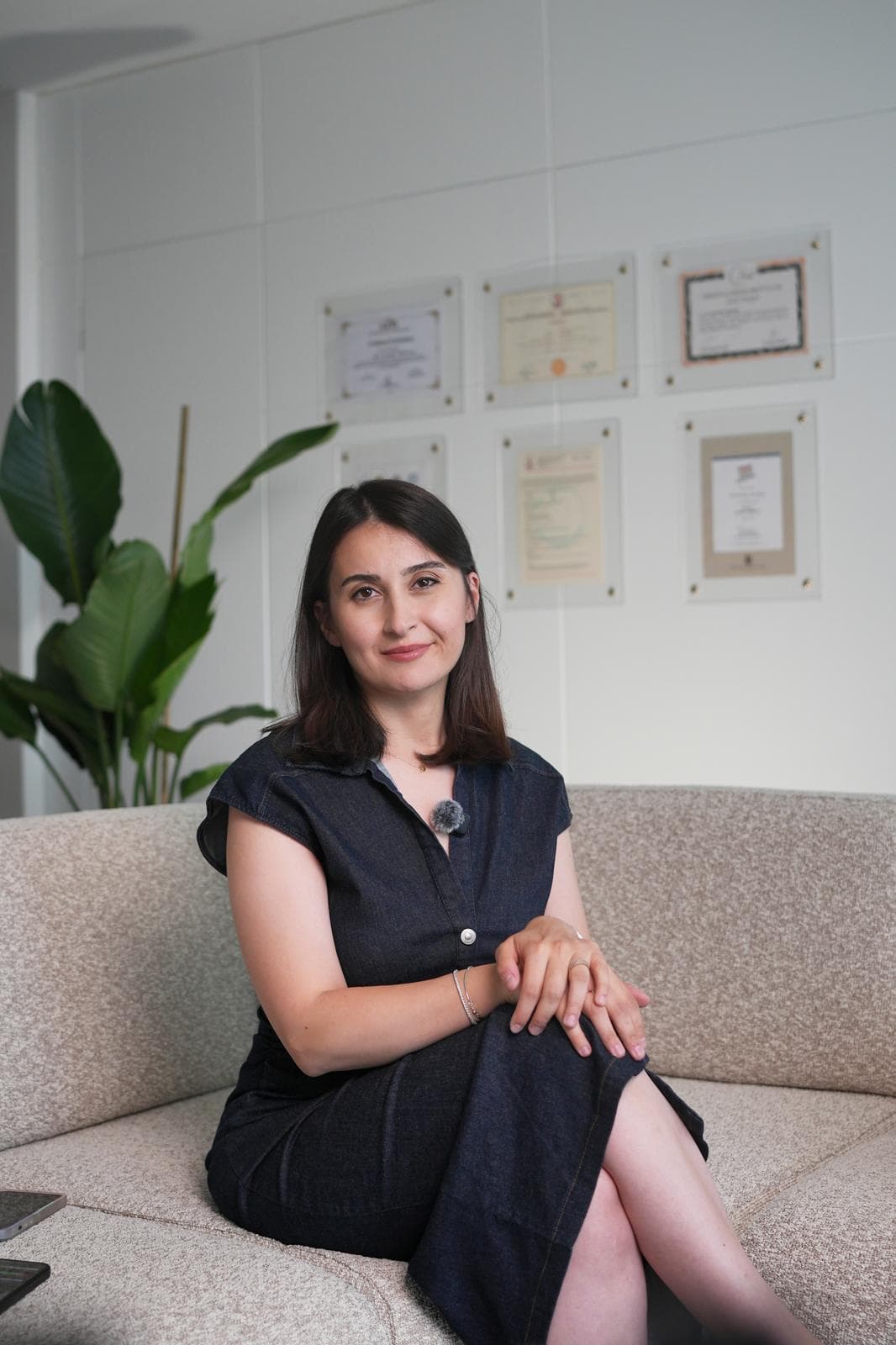 Uzm. Dr. Seda Kanoğlu Yüksekkaya — kliniğindeki sertifika duvarının önünde